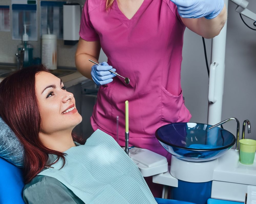 A young redhead woman having examination while sitting in a dental chair in the clinic. A young smiling woman having examination while sitting in a dental chair in the clinic.